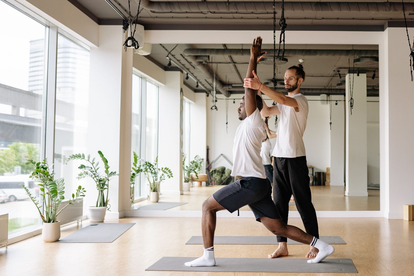 A yoga teacher guiding a practitioner through movement in a bright studio